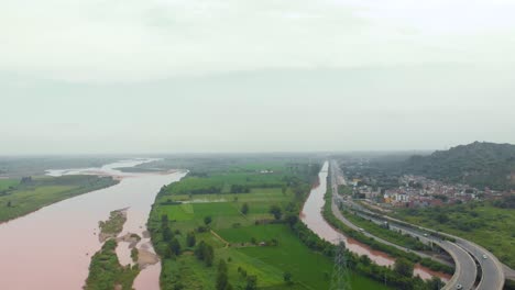 Luftaufnahme-Der-Überführung-über-Ackerland-In-Der-Nähe-Des-Flusses-Und-Des-Kanals-Nach-Regen-Mit-Regnerischem,-Schlammigem-Wasser-Außerhalb-Der-Stadt-In-Der-Region-Punjab,-Indien