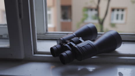 Handheld-shot-of-Black-binoculars-placed-on-open-white-window,-overcast-day