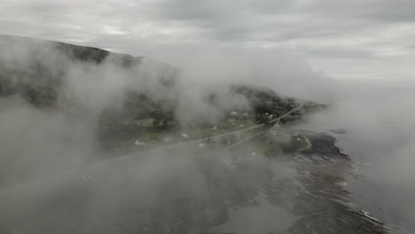Blick-Durch-Düsteren-Nebel-über-Das-Malerische-Grüne-Chic-Chocs-Küstendorf,-Drohnenbahn-Mit-Neigung-Nach-Unten