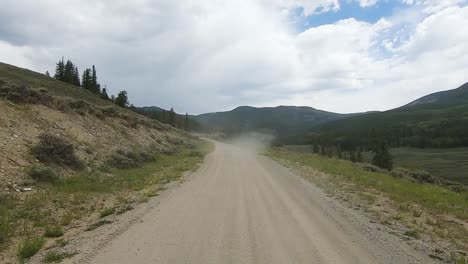 POV-thru-rear-window-while-driving-on-dusty-gravel-road-thru-an-alpine-meadow-in-the-Rocky-Mountains-of-Colorado,-USA