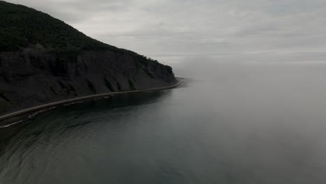 Drone-Descends-through-Cold-Foggy-Ocean-Mist-to-Reveal-Dark-Mountain-and-Cliffy-Coast-Line
