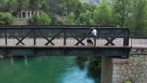 Young-woman-and-her-dog-walking-over-an-old-iron-bridge,-Lago-de-Bolarque
