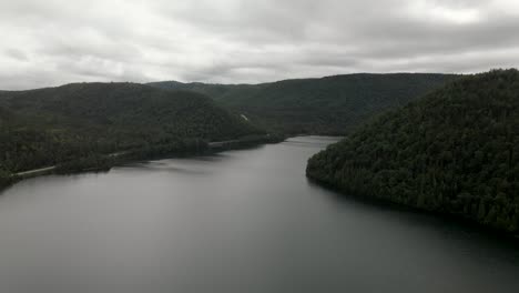 Dark-Clouds-Overcasting-On-The-Calm-Lake-And-Lush-Forest-In-Gaspe-Peninsula,-Quebec,-Canada---aerial-drone