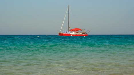 Red-catamaran-floats-near-shore-of-Ionian-sea-with-blue-turquoise-water-on-summer-vacation-day