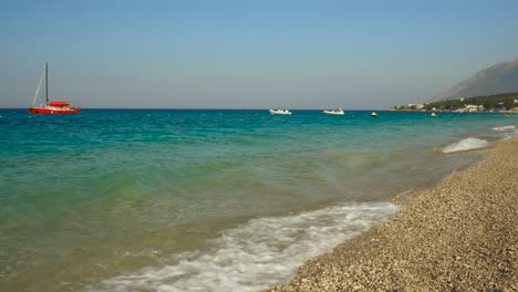 Anchored-boats-and-yachts-near-peaceful-beach-washed-by-clear-turquoise-sea-water-in-Ionian-coastline