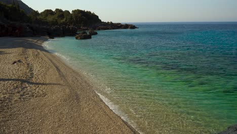 Blue-turquoise-sea-water-washing-pebbles-of-paradise-rocky-beach-in-Ionian-coastline,-Albania