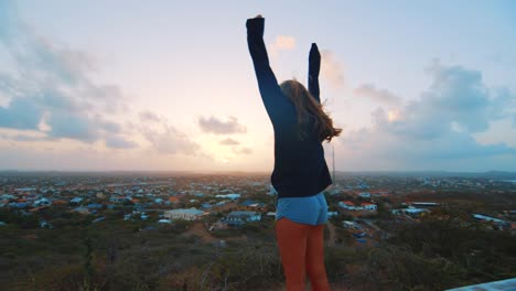Girl-outstretching-arms,-view-of-sunrise-over-Curacao,-Caribbean,-SLOW-MOTION