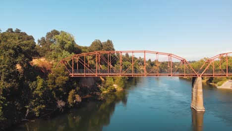 Drone-flying-over-the-American-River-towards-the-red-Fair-Oaks-Bridge-as-a-man-is-crossing-by