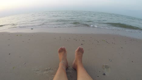 Sitting-by-the-beach,-looking-out-at-the-ocean-over-legs-and-feet