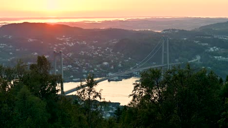 View-from-high-on-a-hill-overlooking-the-Askoy-Bridge-at-sunset-with-red-and-golden-light-on-the-horizon-and-reflecting-on-the-water-in-the-distance