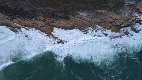 Aerial-of-waves-breaking-on-rugged-South-African-coastline,-Kleinmond,-Overstrand,-South-Africa