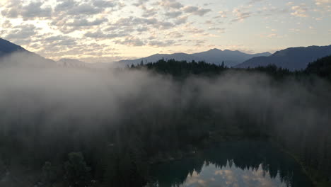 Thick-Fog-Above-Lush-Pine-Forest-And-Lake-Of-Caumasee-Switazerland---aerial-shot
