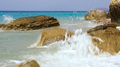 Rocks-splashed-by-white-waves-with-blue-turquoise-sea-water-background-in-Mediterranean