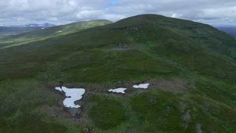 Orbiting-drone-footage-showing-a-Swedish-mountain-top-while-revealing-a-small-lake-in-the-far-distance-behind-it
