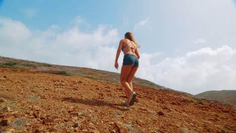 Following-behind-girl-hiking-mountain-in-shorts-and-bikini-top,-low-angle-slowmo