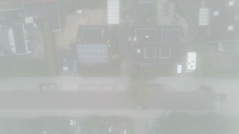 Top-down-aerial-of-cars-driving-over-mist-covered-road-in-suburban-neighbourhood