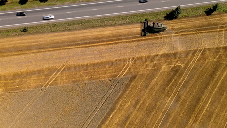 Aerial-top-down-shot-of-combine-harvester-working-on-field-beside-road-with-driving-cars