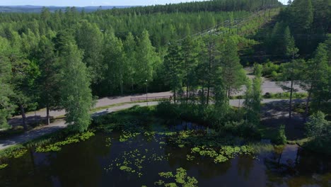 Tracking-drone-footage-over-a-small-lake-showing-two-runners-on-a-gravel-path