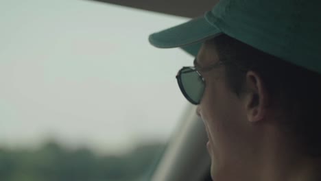 [CLOSE-UP]-shot-from-the-rear-of-a-car-of-a-young-man-wearing-a-blue-cap-and-a-man-bun-singing-and-moving-his-head-to-music