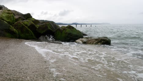 Powerful-splashing-ocean-tide-waves-breaking-wild-overcast-coastal-rocky-shoreline-low-angle