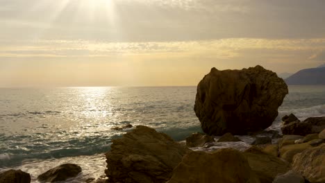 Seascape-at-twilight-with-sun-rays-flares-on-sea-surface-seen-through-rocky-beach-in-Mediterranean