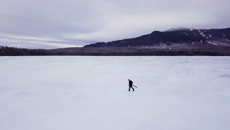 A-man-carries-an-ice-auger-across-frozen-Fitzgerald-Pond,-Maine