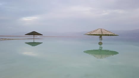 Smooth-dolly-move-over-The-Dead-Sea-very-close-to-the-water-passing-through-a-canopy-umbrella