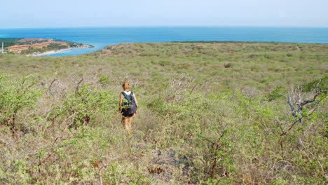 Young-woman-hiking-downhill-towards-Caribbean-Sea-in-Curacao