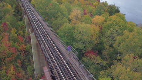 Lone-traveler-standing-on-train-tracks-with-autumn-trees-and-lake-Onawa-in-the-distance