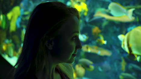 An-attractive,-young-woman-gazing-at-the-fish-in-an-acquarium