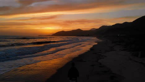 Luftdrohne-Vor-Der-Kalifornischen-Küste-Bei-Sonnenuntergang-Mit-Leuchtend-Orangefarbenem-Himmel-Und-Personensilhouette-Am-Strand