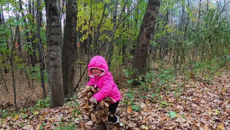 Little-girl-in-pink-hooded-jacket-dramatically-throws-leaves-into-the-air-in-the-forest-SLOW-MOTION