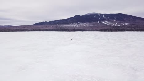 A-lone-snowmobile-treks-across-the-frozen-surface-of-Fitzgerald-Pond,-Maine