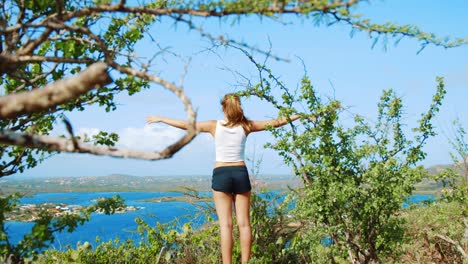 Girl-with-arms-outstretched-up-high-with-view-of-Caribbean-bay