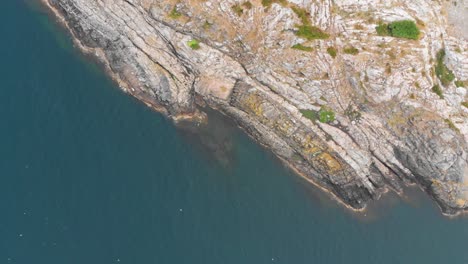Aerial-shot-of-craggy-rocks-coming-out-of-clear-blue-water-with-sparse-vegetation