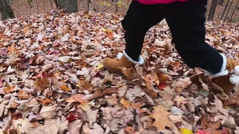 Close-up-of-little-girl's-leather-boots-with-faux-fur-as-she-runs-through-an-autumn-forest-SLOW-MOTION