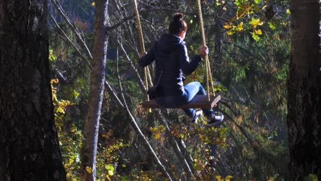 Brunette-girl-swings-in-forest-trail-rope-swing-in-sunny-autumn-day