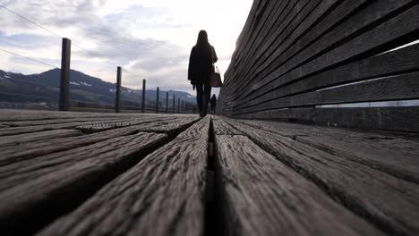 Camera-lock-down-shot-low-on-the-ground-of-a-young-asian-woman-walking-on-a-wooden-pier