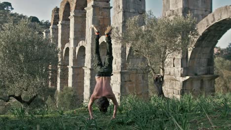 Young-fit-man-does-handstand-press-outdoors-in-front-of-ancient-aqueduct