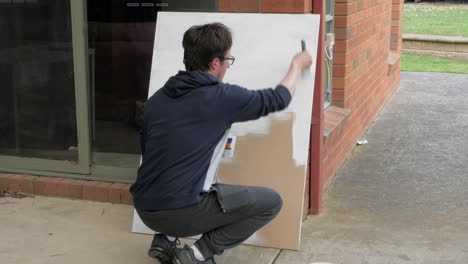 Man-painting-a-board-white-with-undercoat-paint