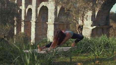 fit-yoga-girl-performs-routine-exercise-within-wilderness-at-Ancient-aqueduct