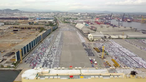 Aerial-view-of-logistics-concept-of-commercial-vehicles,-cars-and-pickup-trucks-waiting-to-be-load-on-to-a-roll-on-roll-off-car-carrier-ship