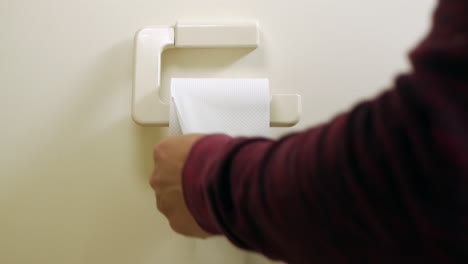 Mann-Zieht-Etwas-Toilettenpapier-Von-Der-Rolle,-Die-An-Der-Wand-Hängt