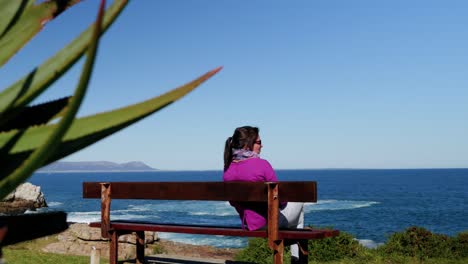 Pensive-woman-sitting-on-bench-looking-out-over-ocean