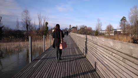 Following-shot-of-a-young-asian-woman-with-black-clothes-walking-on-a-pier-in-slow-motion-in-Rapperswil-Switzerland