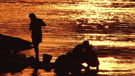 Telephoto-shot-of-a-family-bathing-and-washing-clothing-in-a-river-silhouetted-by-the-sunset