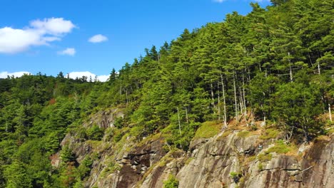 Aerial-footage-Pull-back-from-lone-climber-at-the-top-of-cliff-in-Maine-revealing-blue-skies-and-clouds