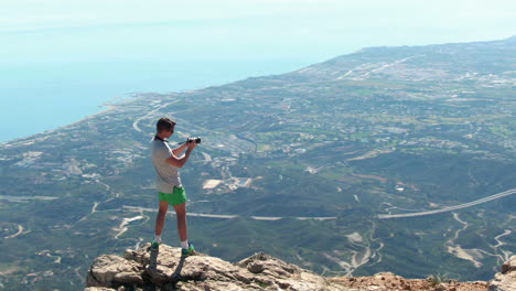 Disparo-De-Arco-Lento-De-Un-Excursionista-Masculino-Tomando-Fotos-De-Marbella-Desde-La-Cima-De-La-Montaña-La-Concha,-Mientras-Sus-Amigos-Miran