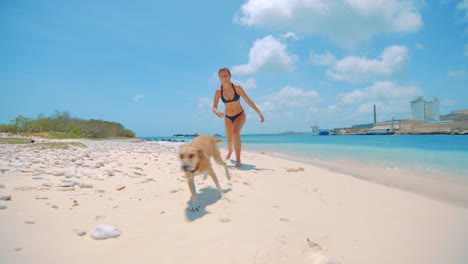 A-young-woman-and-a-dog-running-towards-the-camera-on-a-beach-in-Curacao
