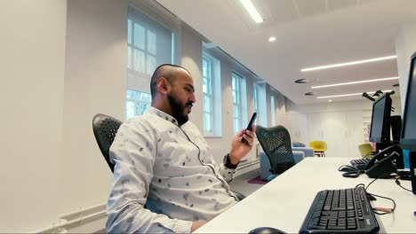 Asian-Indian-male-checking-mobile-phone-whilst-swivelling-on-chair-in-the-office